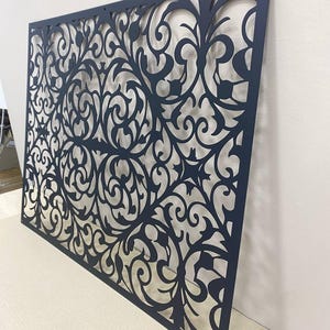 Può includere: Un pannello rettangolare in metallo blu scuro con un intricato motivo tagliato al laser di viticci e disegni floreali simmetrici. La lastra piatta presenta piccoli fori di montaggio agli angoli e un design traforato continuo.