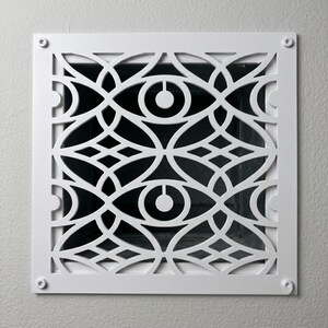 May include: A square white metal air vent cover featuring a repeating geometric pattern of interlocking circles and eye-shaped cutouts. The decorative grille is secured at each of the four corners with a small, visible silver-toned metal screw.