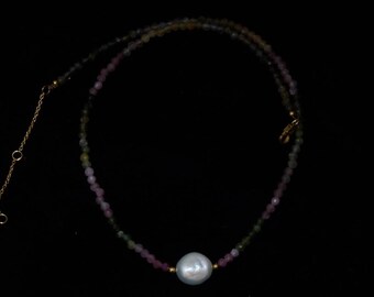 Könnte beinhalten: Eine zarte Halskette aus kleinen rosa, grünen und braunen Perlen mit einem großen Perlenanhänger in der Mitte.