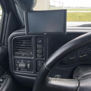 May include: Interior view of a vehicle dashboard. A black steering wheel is in the foreground. A digital display screen is mounted above the dashboard. An air/fuel ratio gauge is mounted above the screen.