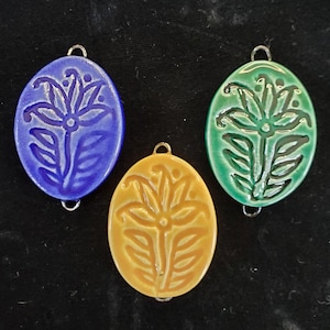 May include: Three ceramic oval-shaped pendants with a floral design. The pendants are blue, green, and yellow.