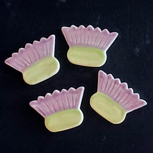 May include: Four ceramic flower tiles in shades of purple and green. The tiles are shaped like stylized flowers with a rounded center and a frilly edge.