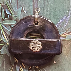 May include: A dark blue ceramic pendant with a silver flower design and a silver loop for hanging.