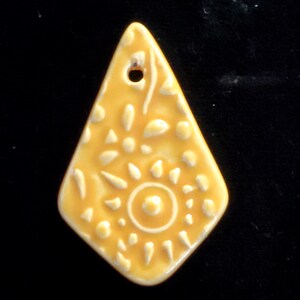 May include: A yellow ceramic pendant with a floral design. The pendant is shaped like a diamond and has a hole at the top for hanging.