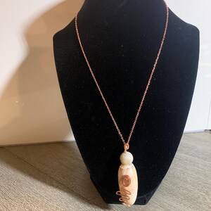 Puede incluir: Un collar de cadena de cobre con un colgante de piedra blanca envuelto en alambre de cobre.