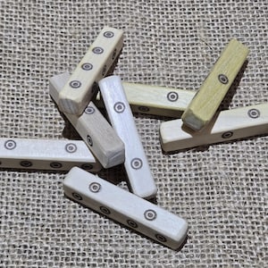 Puede incluir: Un conjunto de piezas de juego de madera con círculos negros en ellas. Las piezas están dispuestas en una pila sobre una superficie de arpillera marrón.