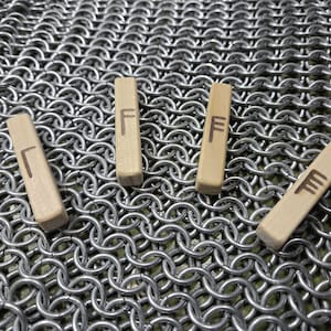May include: Four wooden rune sticks with the rune "Fehu" carved on each. The sticks are arranged in a row on a silver chainmail background.