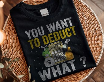 May include: Black t-shirt with the text "YOU WANT TO DEDUCT WHAT?" in silver and yellow. The graphic includes a calculator, money bags, and a receipt. The shirt is folded on a woven basket.