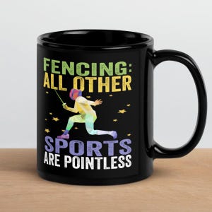 May include: Black coffee mug with the text "FENCING: ALL OTHER SPORTS ARE POINTLESS" and a colorful geometric illustration of a fencer. The mug has a large handle and is suitable for hot or cold beverages.