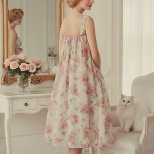May include: A woman in a floral print dress with pink rose patterns, standing in a room with a vintage mirror and a white cat. The dress has a pink trim and is knee-length. A "Print at Home PDF Sewing Pattern" logo is visible.