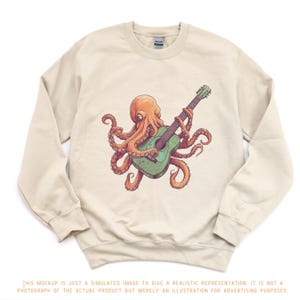 Puede incluir: Sudadera beige con una ilustración de un pulpo naranja tocando una guitarra verde. El pulpo es el elemento central del diseño. La imagen incluye un descargo de responsabilidad en la parte inferior, que indica que es una imagen simulada.