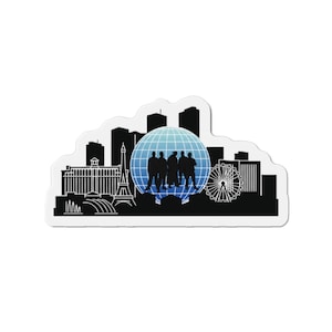 Pode incluir: Um autocolante recortado com uma silhueta de paisagem urbana a preto e branco, incluindo a Torre Eiffel e uma roda gigante. Um globo azul com um grupo de pessoas está no centro. O autocolante tem uma borda branca.