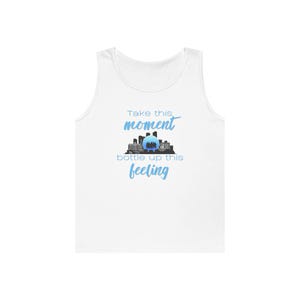 Puede incluir: Una camiseta sin mangas blanca con el texto "Take this moment bottle up this feeling" en letras azules claras. Centrado entre las líneas hay una silueta negra de un horizonte urbano con un orbe circular azul claro brillante en el centro.