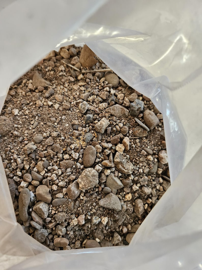 May include: A close-up of a plastic bag filled with a mixture of small and large rocks, gravel, and dirt. The rocks are various shades of brown, gray, and white.