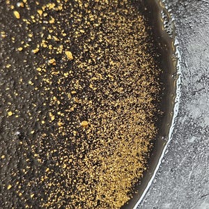 May include: Close-up of a black and silver resin art piece with gold flecks. The resin has a smooth, glossy finish and the gold flecks are scattered throughout the piece.
