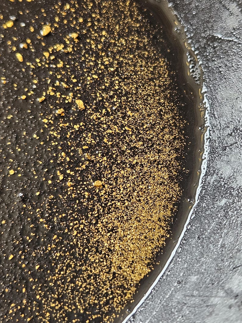May include: Close-up of a black and silver resin art piece with gold flecks. The resin has a smooth, glossy finish and the gold flecks are scattered throughout the piece.