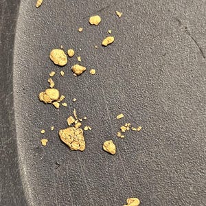 May include: A close-up of a black pan with small, irregular pieces of gold scattered across the surface.