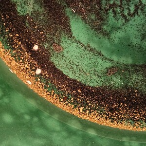 May include: A close-up of a green pan with a layer of black and gold specks. The gold specks are concentrated around the edge of the pan.