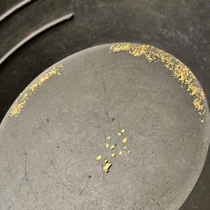 May include: A close-up of a black pan with small, shiny gold flakes scattered across the bottom.