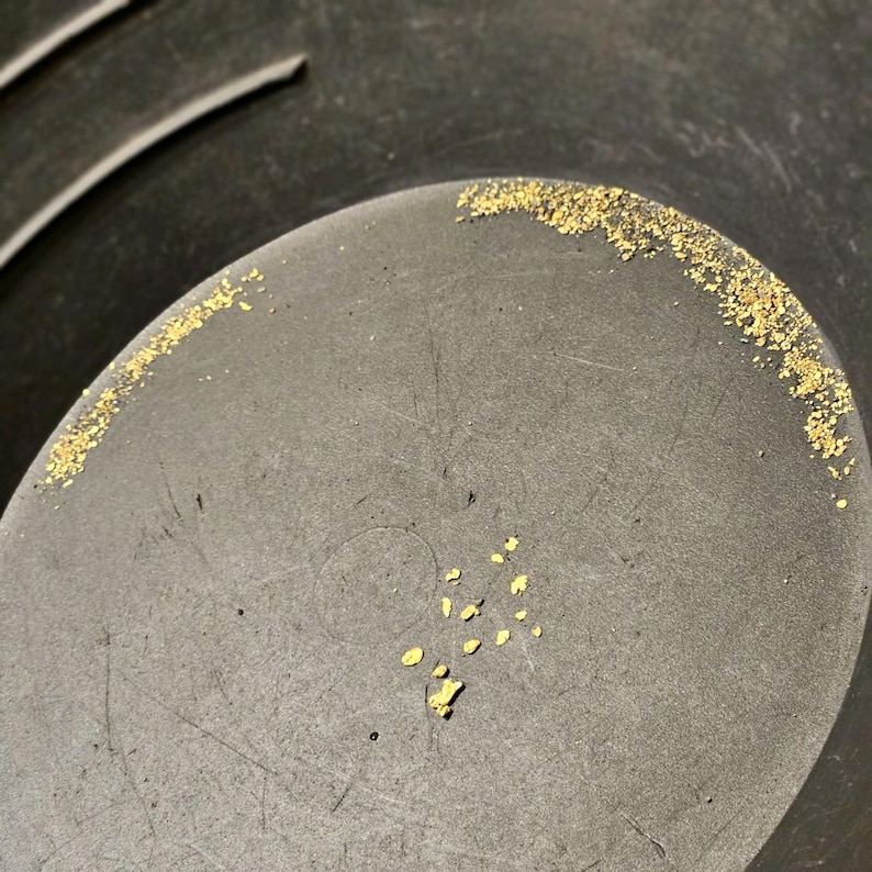 May include: A close-up of a black pan with small, shiny gold flakes scattered across the bottom.