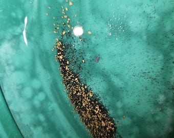 May include: A close-up of a green pan with a small pile of gold flakes and black sand in the bottom.