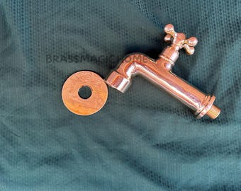 May include: A polished brass faucet with a cross-shaped handle and a round, copper-colored washer. The faucet is angled and has a threaded end. The text "BRASSMAGICHOME" is visible.