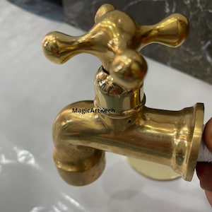 Può includere: Un rubinetto in ottone dorato con una maniglia a forma di croce. Il rubinetto è progettato per l'uso esterno e ha una connessione filettata.
