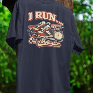 Puede incluir: Camiseta azul marino con un diseño retro que presenta zapatillas para correr, un cronómetro y el texto "I Run Out of Motivation". El gráfico es en tonos de rojo, blanco y azul.