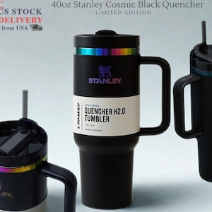 May include: Three black Stanley Cosmic Black Quencher tumblers with handles and straws. The tumblers have a rainbow iridescent band near the top and the text "STANLEY" is visible. The largest tumbler is labeled "40oz" and "QUENCHER H2.0 TUMBLER".