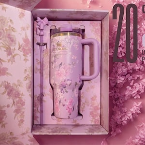 May include: A light purple Stanley tumbler with a floral pattern, a matching handle, and a straw, presented in a decorative box with a floral interior. The text 20% OFF ON ALL PRODUCTS is visible on the right side of the image.