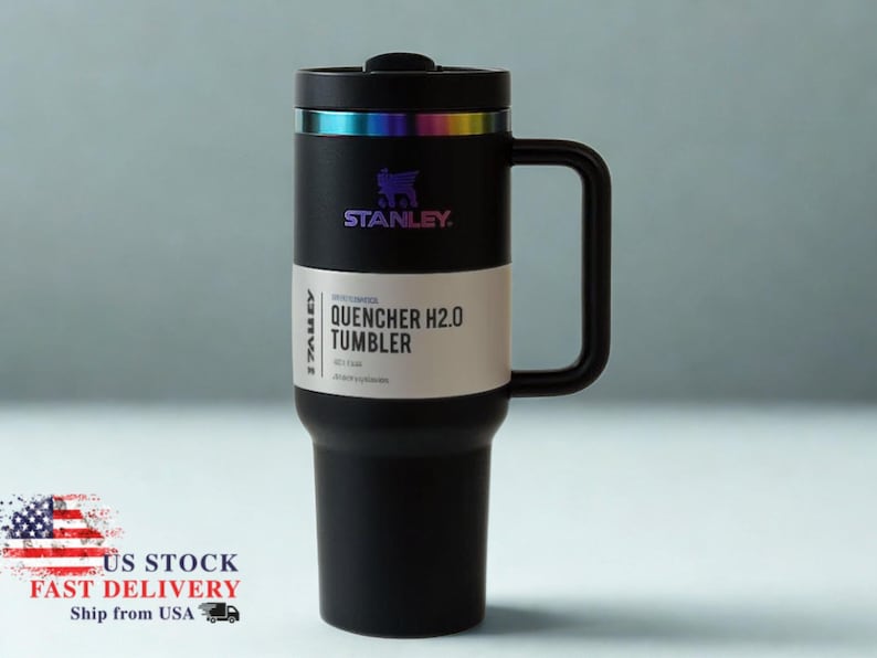 May include: Black Stanley Quencher H2.0 tumbler with a handle. The tumbler has a black lid with a rainbow-colored band and the Stanley logo. The text "QUENCHER H2.0 TUMBLER" is printed on a white label. The tumbler is designed to keep drinks cold.
