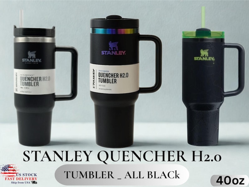 May include: Three black Stanley Quencher H2.0 tumblers with handles and straws. The left and center tumblers feature white product labels reading Quencher H2.0 Tumbler. The center tumbler has an iridescent rim. The right tumbler has a green lid.