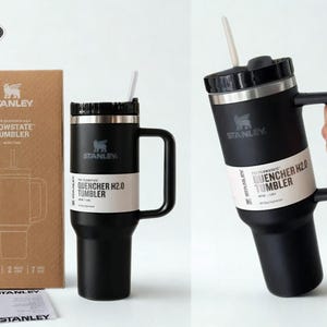 May include: A matte black Stanley Flowstate Quencher H2.0 tumbler with a handle, a black lid, and a white straw. The tumbler features a white product label and is shown next to its brown cardboard packaging box, which displays the Stanley logo and text.