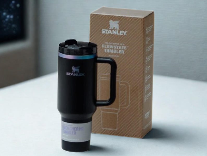 May include: A black Stanley Flowstate tumbler with a handle and a matching box. The tumbler has a black lid with a silver rim and the Stanley logo. The box is brown with the Stanley logo and product information.