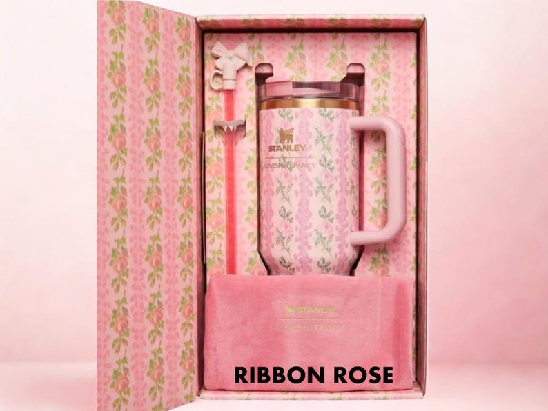 Puede incluir: Un termo Stanley rosa con un estampado floral, una pajita a juego y una bolsa de terciopelo rosa, presentado en una caja decorativa. La caja y el termo muestran el texto "Ribbon Rose".