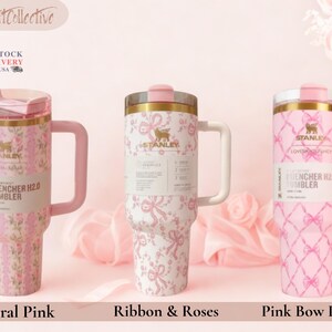 May include: Three Stanley Quencher H2.0 tumblers with handles and lids. The left tumbler features a pink floral pattern, the center tumbler has a pink ribbon and rose design, and the right tumbler displays a pink bow lattice pattern.