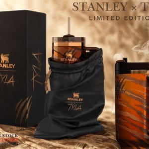 May include: A limited edition Stanley x Tyla gift set. The set includes a black box, a tumbler in a black drawstring bag, and a mug with a tiger stripe design. The Stanley logo and the word "Tyla" are visible on the box and the bag.