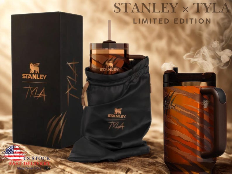 May include: A limited edition Stanley x Tyla gift set. The set includes a black box, a tumbler in a black drawstring bag, and a mug with a tiger stripe design. The Stanley logo and the word "Tyla" are visible on the box and the bag.