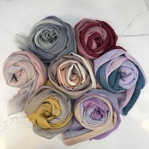 Può includere: Una collezione di otto sciarpe ombré in vari colori, tra cui rosa, viola, blu, verde e giallo. Le sciarpe sono arrotolate e disposte in cerchio.