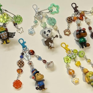 May include: Five colorful keychains featuring various character figurines. Each keychain has a different color clasp and is adorned with beads, charms, and decorative elements. The figurines include an owl, a dog, a raccoon, a monkey, and a dog-like character.