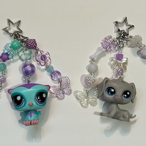 May include: Two keychains with star-shaped clasps. One features a teal owl figurine with purple accents and a beaded strand. The other has a gray puppy figurine and a beaded strand with a paw charm.