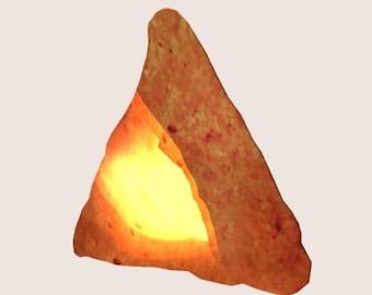 May include: A triangular shaped lamp made from a single piece of orange-brown rock salt. The salt is carved to create a hollow space in the center of the lamp, which is illuminated by a warm yellow light.