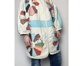 Puede incluir: Chaqueta acolchada color crema con diseños florales de patchwork coloridos. La chaqueta presenta una franja horizontal azul claro y mangas abullonadas. Una prenda de abrigo única de inspiración vintage.