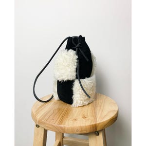 Puede incluir: Un bolso de cubo negro y blanco con cierre de cordón y una correa larga. El bolso está hecho de gamuza y piel sintética.