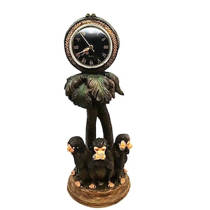 May include: A decorative clock shaped like a palm tree with three monkeys at the base. The monkeys are covering their eyes, ears, and mouth. The clock face is black with Roman numerals and gold hands.