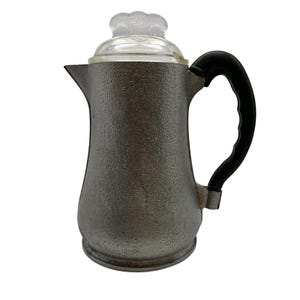 May include: A silver aluminum coffee pot with a black plastic handle and a clear glass lid. The pot has a textured surface.