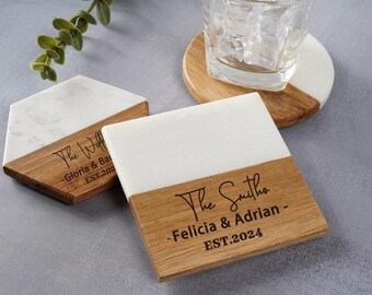 Op de afbeelding: Twee witte marmeren en houten onderzetters met gepersonaliseerde tekst. De eerste onderzetter zegt "The Williams - Gloria & Barry - EST.2021". De tweede onderzetter zegt "The Smiths - Felicia & Adrian - EST.2024".