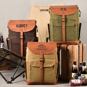 Puede incluir: Tres mochilas de lona personalizadas con detalles de cuero. Las mochilas son de color marr&oacute;n, verde y beige. Las mochilas tienen correas y hebillas de cuero. Las mochilas est&aacute;n personalizadas con los nombres Aubrey, RK y Vincent.