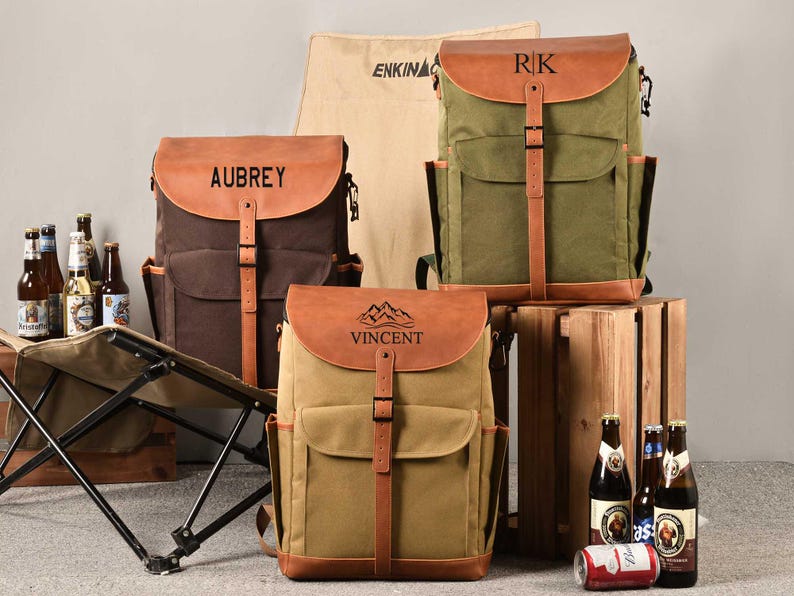 Puede incluir: Tres mochilas de lona personalizadas con detalles de cuero. Las mochilas son de color marr&oacute;n, verde y beige. Las mochilas tienen correas y hebillas de cuero. Las mochilas est&aacute;n personalizadas con los nombres Aubrey, RK y Vincent.