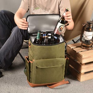 Puede incluir: Una mochila enfriadora de lona verde con detalles en cuero marr&oacute;n y un bolsillo frontal con cremallera. El enfriador est&aacute; lleno de seis botellas de cerveza.